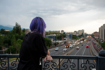 Fototapeta na wymiar Teenager with purple hair is watching evening highway on the bridge
