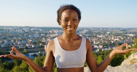 Mindful girl sitting cross-legged at the mountain, practicing yoga and enjoying meditation. Young woman with pleasure smile meditating at the nature
