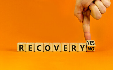 Recovery symbol. Businessman turns a wooden cube and change words 'recovery no' to 'recovery yes'. Beautiful orange background. Business and recovery concept, copy space.