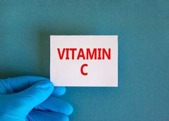 Vitamin C symbol. White note with words Vitamin C, beautiful blue background, doctor hand in blue glove. Medical, vitamin C concept.