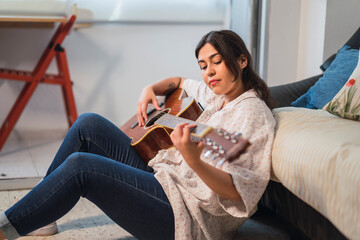 Chica joven guapa con guitarra acustica tranquilamente sentada en el suelo en su casa