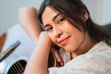 Chica joven guapa con guitarra acustica tranquilamente sentada en el suelo en su casa