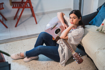 Chica guapa con guitarra acústica tranquila en el salón de su casa