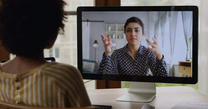 Over Shoulder Back View Of Millennial Black Female Focused On Pc Screen Talking To Young Indian Woman Friend From Abroad By Video Call. Two Diverse Ladies Having Online Conversation In Messenger App