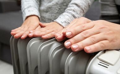 Mother and son warms hands above the electric oil radiator
