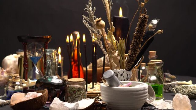Occult and esoteric witch doctor still life. Halloween background with magic objects. Black candles, human skull, teeth, and potions vials on witch table. Mystic witchery with weeds.