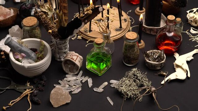 Witchy table arranged with witch craft magic items. Magic mushrooms. Still life with black magic candles, ritual dry weeds, animals bones and green potion vial. Halloween concept.