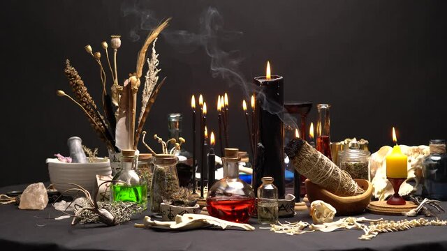 Occult and esoteric witch doctor still life. Halloween background with magic objects. Black candles, skull, bones, and potions vials on witch table. Mystic witchery with weeds.