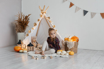Little cute girl playing in a wigwam in her room with autumn decor and pumpkins. Happy childhood concept © Наталья Мокрецова