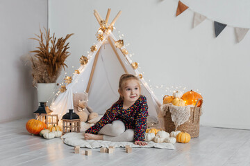 Little cute girl playing in a wigwam in her room with autumn decor and pumpkins. Happy childhood concept © Наталья Мокрецова