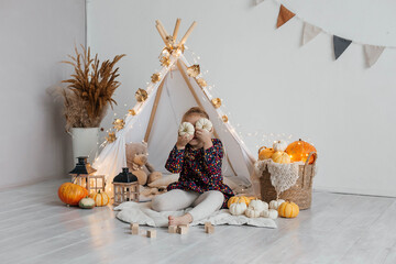 Little cute girl playing in a wigwam in her room with autumn decor and pumpkins. Happy childhood concept © Наталья Мокрецова