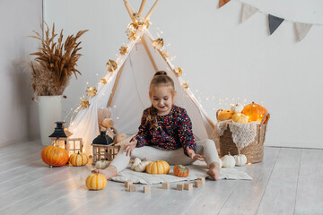 Little cute girl playing in a wigwam in her room with autumn decor and pumpkins. Happy childhood concept © Наталья Мокрецова