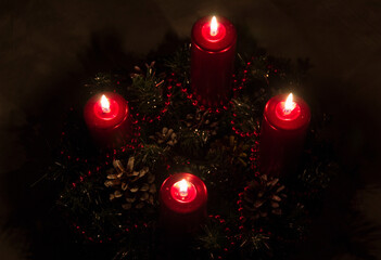 Close up of four red candles burning on advent wreath on evening. Merry Christmas, Advent crown decoration, 4th sunday, Christmas background. Advent wreath with candlelights on table in wintertime