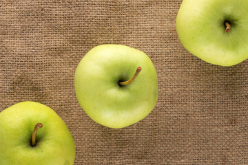 Three ripe sweet apples on burlap, close-up, top view.