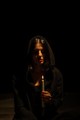 Portrait of mystical looking beautiful woman holding burning candle in hand in darkness with cinematic lighting. Vertical shot.