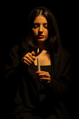 Portrait of attractive woman burning the candles in darkness with cinematic lighting. Vertical shot.