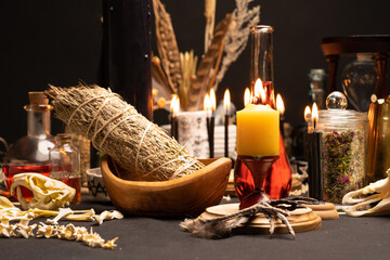 Witch table with witch craft magic items. Selective focus at front. Still life with black magic candles, ritual dry sage weed and animal bones, red potion vials and raven or crow toe. Halloween.