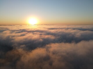 Fototapeta na wymiar Dense fog clouds with the morning sunrise. Clouds formed over a lake approximately 100 feet below the clouds. Image could be drone an airplane window or drone.