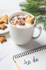 Christmas background. To-do list and festive cocoa with marshmallow on white marble. New Years resolutions concept.