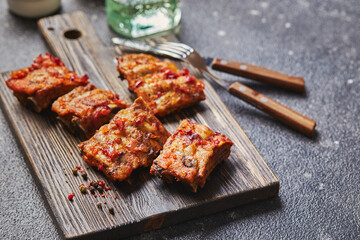 Grilled baked pork ribs with spices on wooden cutting board on dark background. American food concept.