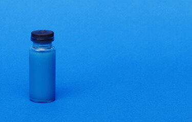 One glass clear bottle with a red vaccine medicine on a blue background.