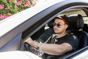 Fototapeta na wymiar a teenager is driving. a modern young guy with sunglasses, fashionable with a beard, drives a white car. driving training or car travel