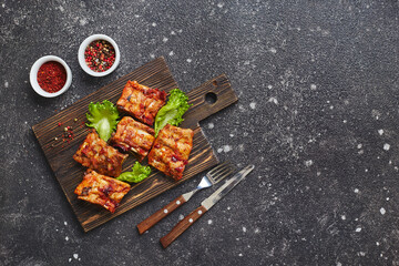 Grilled baked pork ribs with spices and vegetables on wooden cutting board on dark background. American food concept. Top view, copy space.