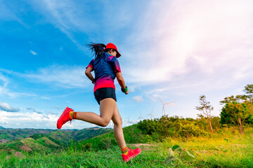 Asian female trail runners, wearing sportswear, are practicing running and jumping on the high mountain. There is a field of wind turbines generating electricity in the background.