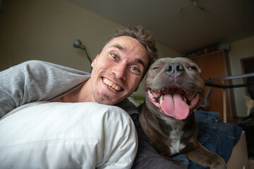 Pleased young man looking at camera and taking selfie with amstaff dog