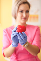 Woman in a pink medical uniform holding a heart in a hands.