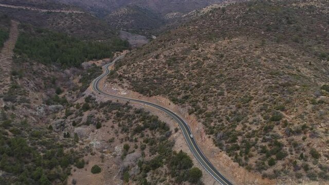 Aerial following vehicle on winding highway through arid mountains, 4K