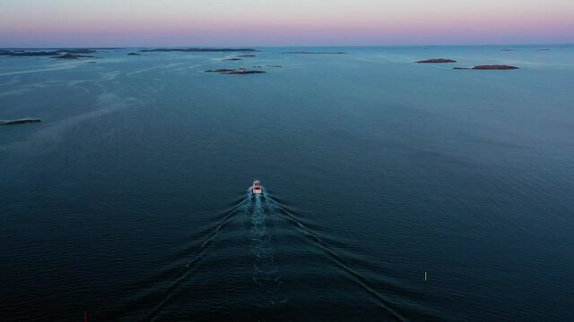 Aerial view of a sunlit boat driving away on tranquil sea water, dusk in Scandinavia - rising, drone shot