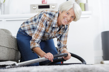 senior woman vacuuming under the sofa - Powered by Adobe