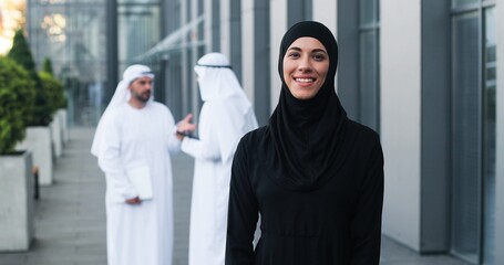 Waist up portrait view of the happy businesswoman wearing head scarf standing at the street at the dinner break and smiling near her office center. Business people concept