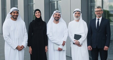 Successful team. Waist up portrait view of the arabian business people standing with their caucasian business partner and smiling at the camera while posing outdoors
