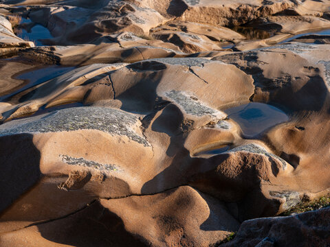 Rounded shapes of eroded bed rock on the west coast of Sweden, Europe. Water pools and shadows.