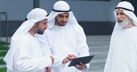 Waist up portrait view of the team of arabian businessmen chatting with each other and looking at...