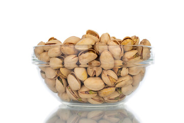 Lots of unpeeled pistachios in a glass dish, close-up, isolated on white.