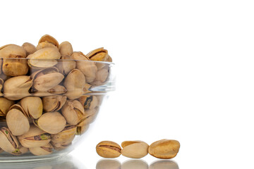 Lots of unpeeled pistachios in a glass dish, close-up, isolated on white.