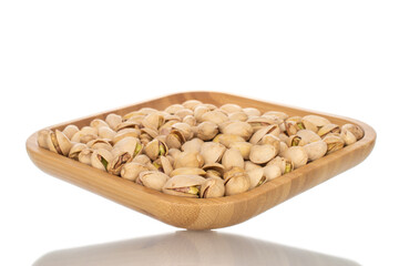 Many unpeeled pistachios in a bamboo dish, close-up, isolated on white.