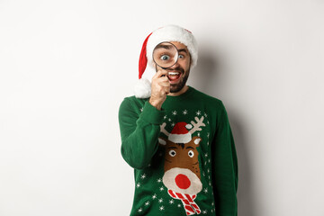 Christmas and holidays concept. Funny bearded guy in Santa hat looking through magnifying glass...