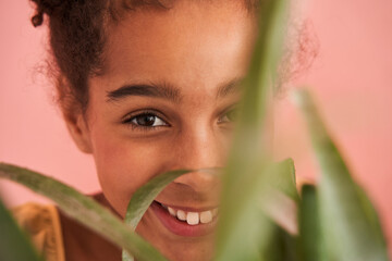 Little black girl behind leaves of green plant