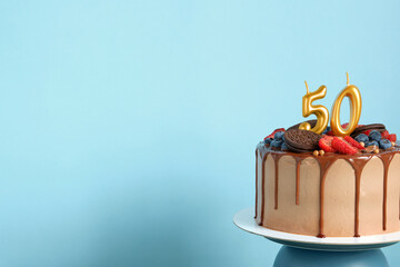 Chocolate birthday cake with berries, cookies and number fifty golden candles on blue wall...