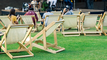 Many empty white deck chairs with tables for dinner in lawn is surrounded by shady green grass....