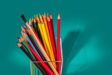 Clear acrylic pot filled with colored pencils of different colors. Blue background. With space for text.