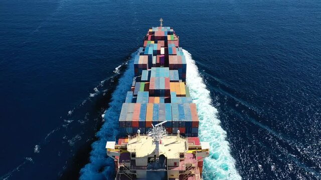 Aerial drone video above huge colourful container carrier vessel cruising deep blue open ocean sea