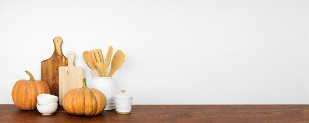 Autumn theme kitchenware and utensils with rustic pumpkins on a wooden shelf or counter. Banner...