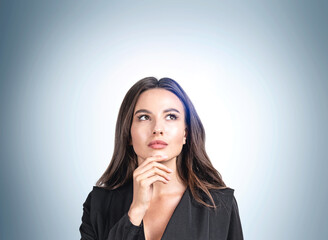 Thoughtful young attractive businesswoman wearing formal suit is standing