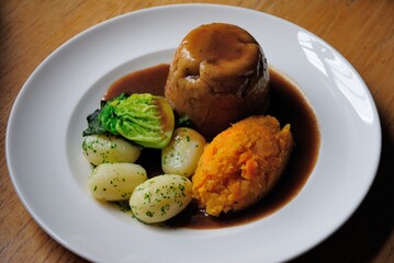 Traditional British Steak and kidney pudding made with stewed beef steak and ox kidney enclosed in suet pastry and served with boiled potatoes, mashed rutabagas (neeps) and greens in Newcastle, UK