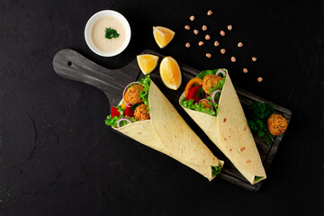 Tortillas wrapped with falafel balls and fresh vegetables, vegetarian healthy food, on a black...